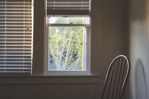 A vertical interior shot of a wooden chair near the window with blinders